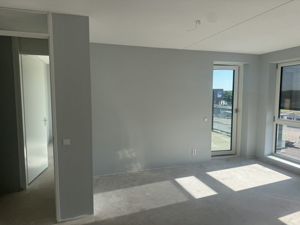 Appartement met lichtgrijs afgewerkte wanden, een balkondeur en zon op de betonvloer