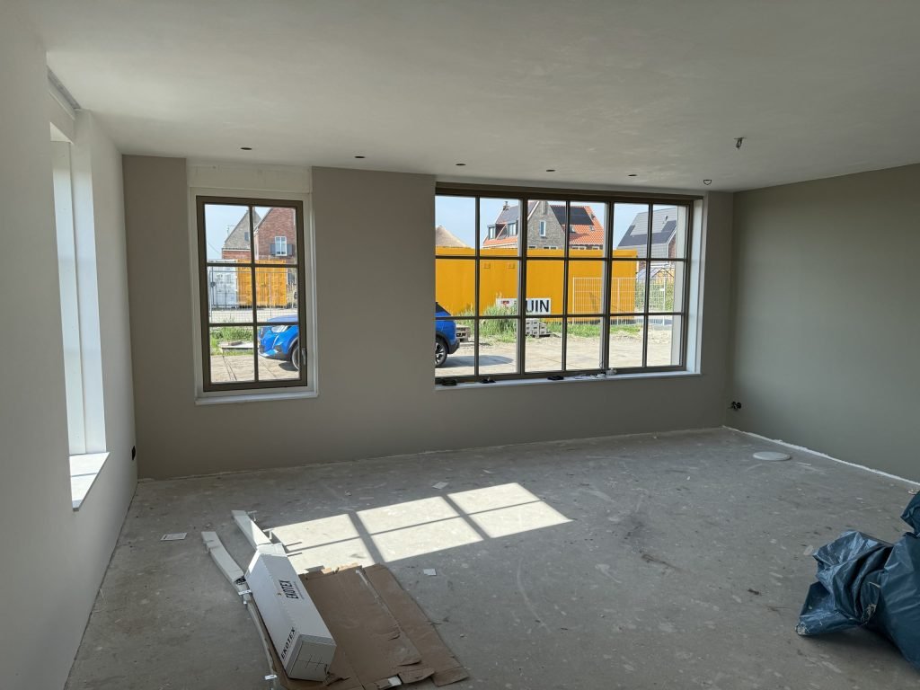 Woonkamer van een nieuwe woning met wanden in een warme grijstint en grote ramen