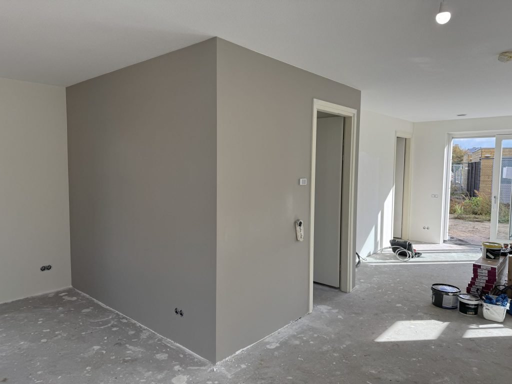 Pas afgewerkte grijze wand in een nieuwe woning, met verfemmers op de vloer